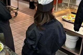 Mitarbeitende der Mensa geben farbenfrohe Bowls an hungrige Studierende aus, während das Küchenteam im Hintergrund aktiv ist.