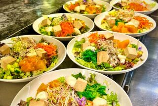 Bunte Bowls mit frischem Gemüse, Tofu und Sprossen stehen auf einer Edelstahlfläche zur Ausgabe in der Mensa des Studierendenwerks Paderborn bereit.
