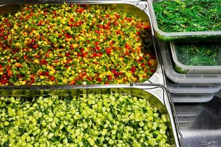 Verschiedene geschnittene Zutaten wie Gurken, Paprika, Karotten, Algen und Pilze sind in Edelstahlschalen und Kunststoffboxen für die Bowl-Zubereitung vorbereitet.