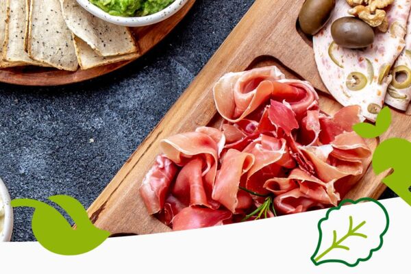 Feinkostplatte mit luftgetrocknetem Schinken, Wurstaufschnitt, Oliven, Nüssen, Crackern und cremigen Aufstrichen auf dunklem Untergrund