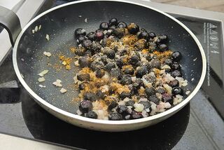 Blaubeeren und Zucker in einer Pfanne auf einem mobilen Herd, umgeben von frischen Erdbeeren und geschnittenen Früchten bei einem Outdoor-Kochkurs
