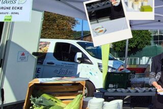 Detailaufnahme des Stands ‚Grüne Ecke‘ von Manss Foodservice mit frischem Gemüse, Obst, Wraps und Schälchen vor einem weißen Zelt beim Sommerfest von Blumen Risse und Overkamp