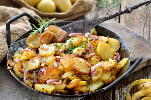 Rustikal servierte Bratkartoffeln in der Pfanne mit Speckstreifen, Zwiebeln und frischen Kräutern.