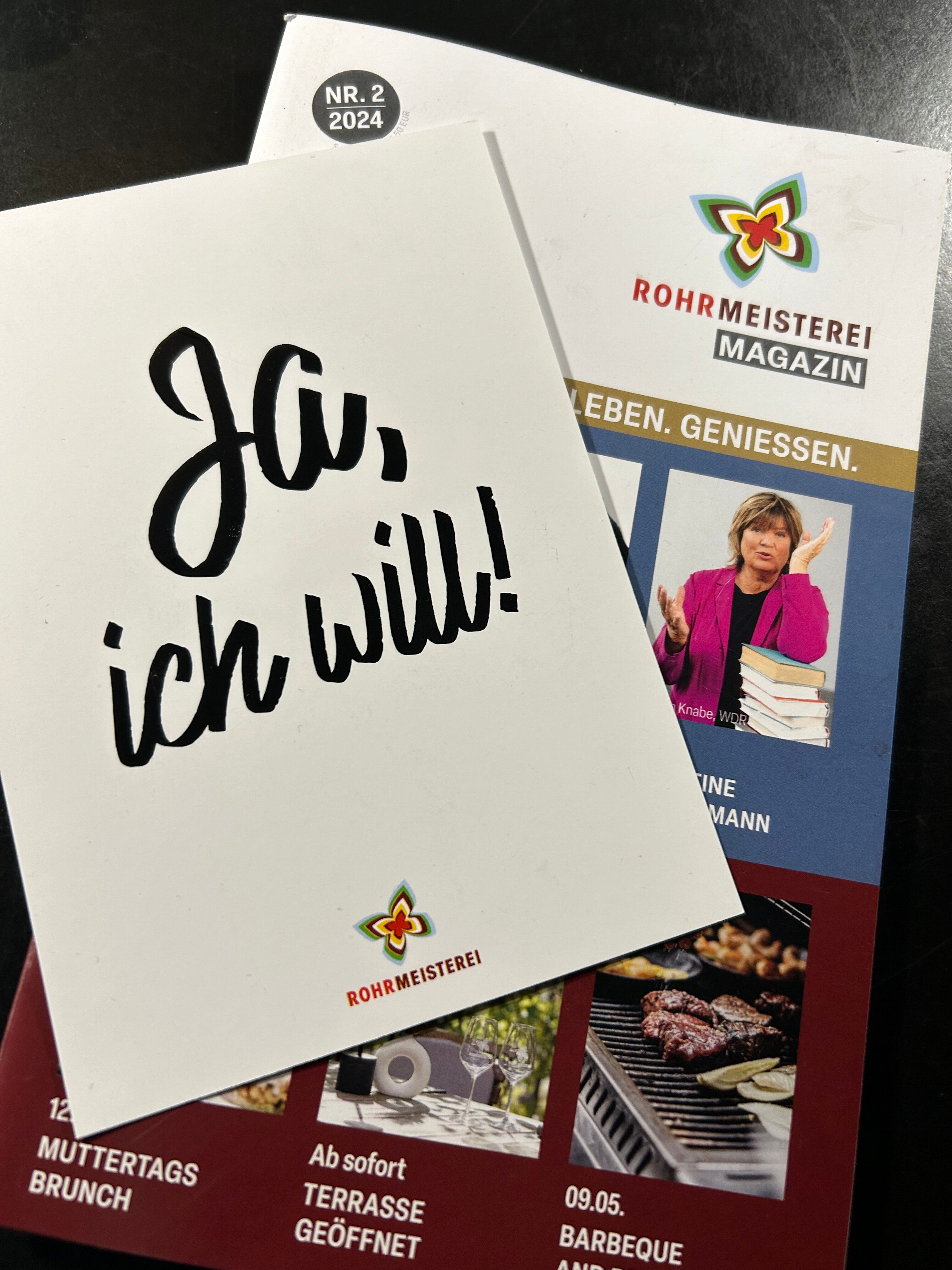 Auf dem Bild sind eine Ausgabe des Rohrmeisterei Magazins sowie eine weiße Postkarte mit der Aufschrift ‚Ja, ich will!‘ zu sehen – beides trägt das Logo der Rohrmeistere