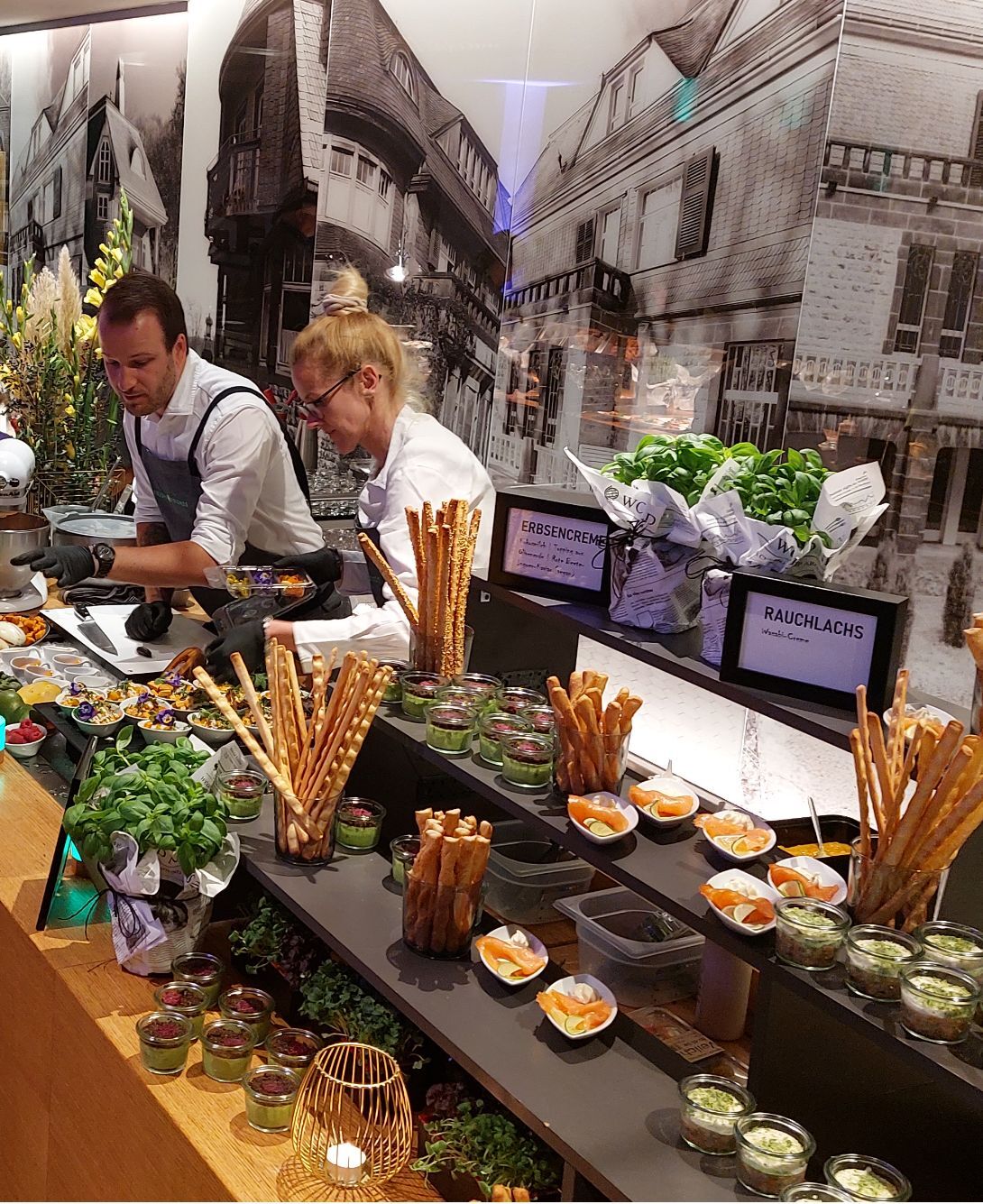 Zwei Mitarbeitende bereiten frische Speisen beim Live-Cooking im Seminarhotel zu, umgeben von Kräutern und Zutaten