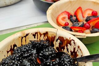 Verschiedene Schalen mit frischen Beeren wie Brombeeren, Erdbeeren, Johannisbeeren und Trauben auf einem grünen Tisch – im Vordergrund ein Beerenmix mit dunkler Sauce, im Hintergrund eine Waage