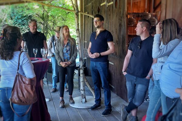Menschen stehen in einer rustikalen Holzscheune bei einem Empfang zusammen – eine Frau und ein Mann begrüßen die Gäste der Waldpilz-Exkursion