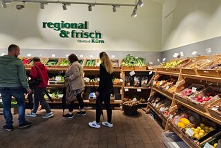 Kundinnen und Kunden beim Einkauf im Hofladen ‚Regional & Frisch‘ vom Obsthof Körn mit einer großen Auswahl an regionalem Obst und Gemüse in Holzregalen