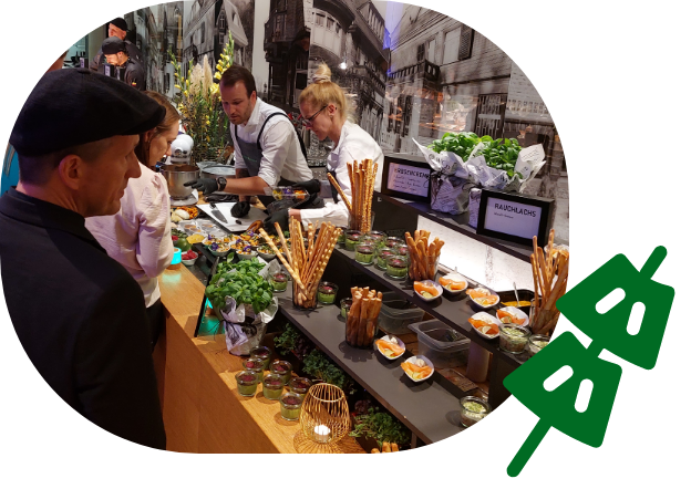 Menschen bei einer Verkostung mit frischen Kräutern, Dips und Fingerfood an einem stilvoll dekorierten Stand.