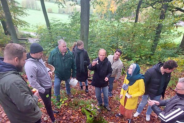 Teilnehmende einer Pilzexkursion stehen im herbstlichen Wald zusammen und tauschen sich über Pilzfunde aus