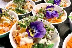 Detailaufnahme einer veganen Bowl mit essbaren Blüten, Microgreens, Karotten und Dressing