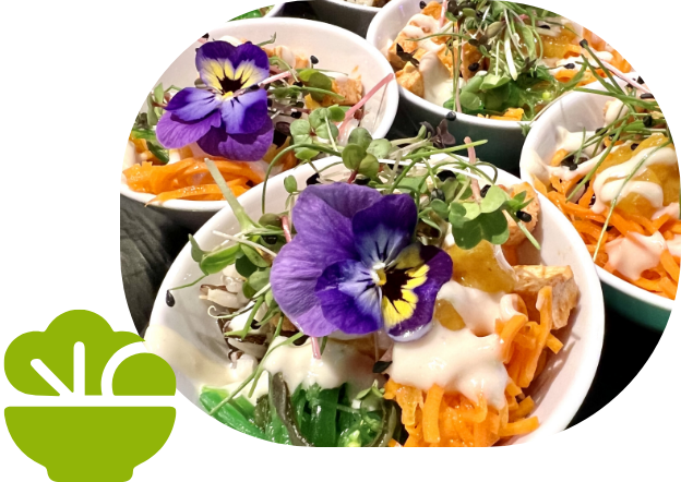 Kleine Schalen mit bunt angerichtetem Salat aus Möhren, Sprossen und violetten Blüten, serviert mit Dressing.