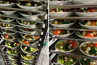 Mehrere vorbereitete Bowls mit frischen Zutaten stehen gestapelt auf einem Rollwagen, bereit zur Ausgabe in der Mensa.