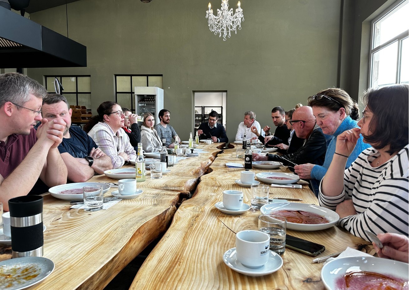 Teilnehmende des Manss-Workshops zur Frühlingsküche sitzen gemeinsam an einer langen Holztafel, genießen die Speisen und tauschen sich in entspannter Atmosphäre aus